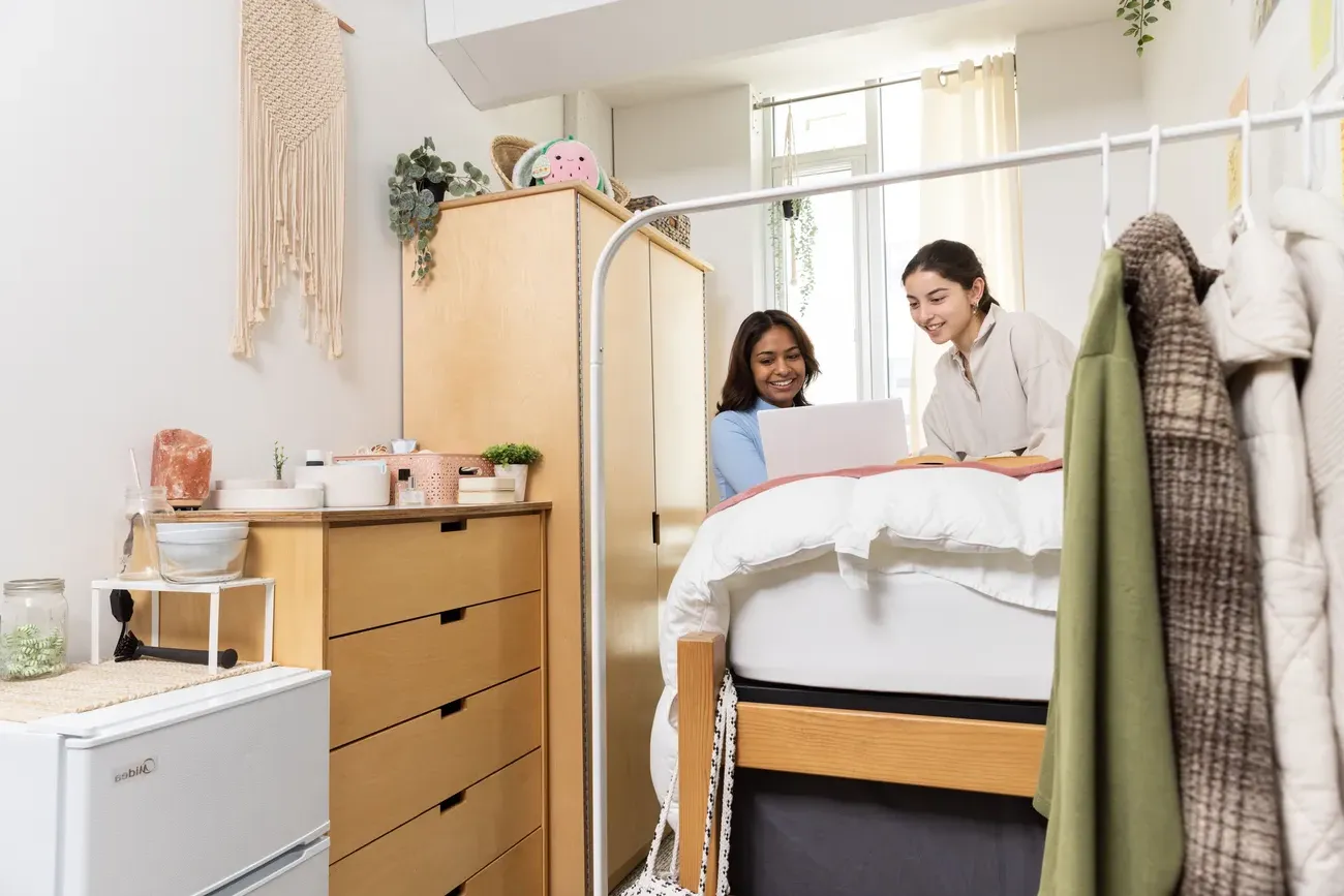 Two students look at a computer in their dorm room together.